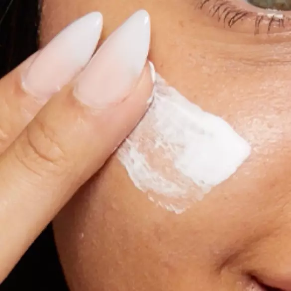 A close-up of a hand applying white cream to the cheek, showcasing smooth skin and manicured nails.
